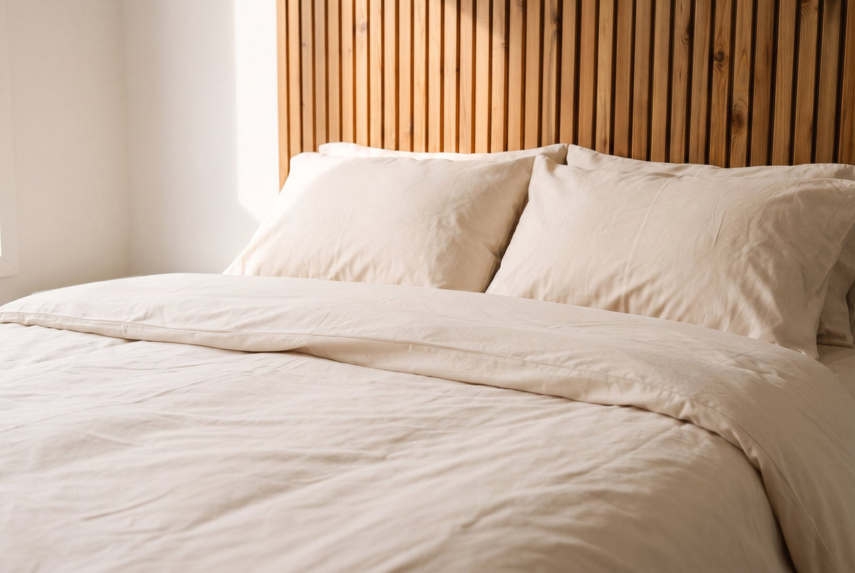 A neatly made bed in Natural cotton bedding against a wood slat headboard